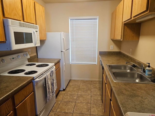 kitchen featuring dark countertops, white appliances, brown cabinetry, and a sink