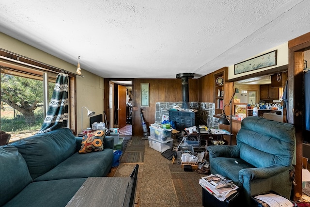 living room with dark carpet, a wood stove, a textured ceiling, and wooden walls