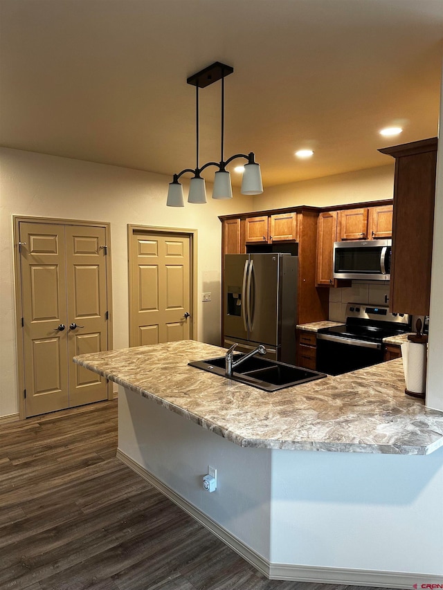 kitchen featuring light stone counters, dark wood-type flooring, sink, hanging light fixtures, and appliances with stainless steel finishes