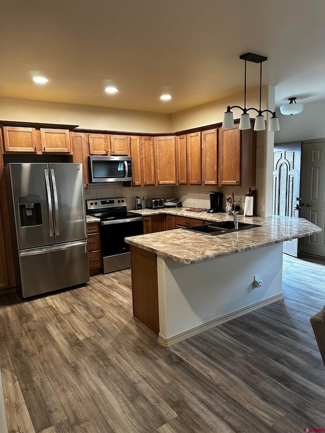 kitchen with hanging light fixtures, kitchen peninsula, stainless steel appliances, wood-type flooring, and sink