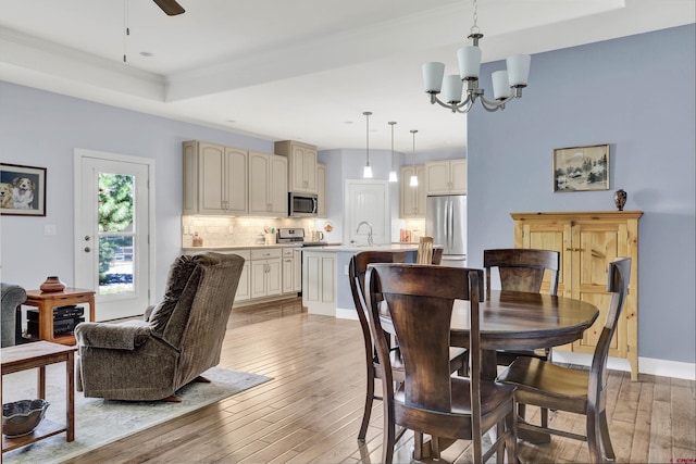 dining room featuring sink, ceiling fan with notable chandelier, a raised ceiling, and light hardwood / wood-style floors