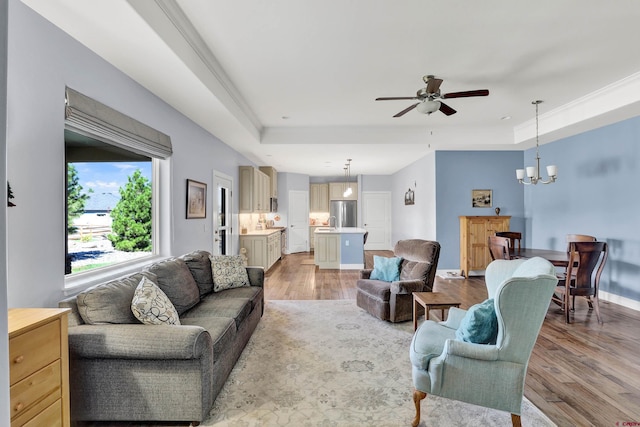 living room with ceiling fan with notable chandelier, light hardwood / wood-style flooring, and a tray ceiling