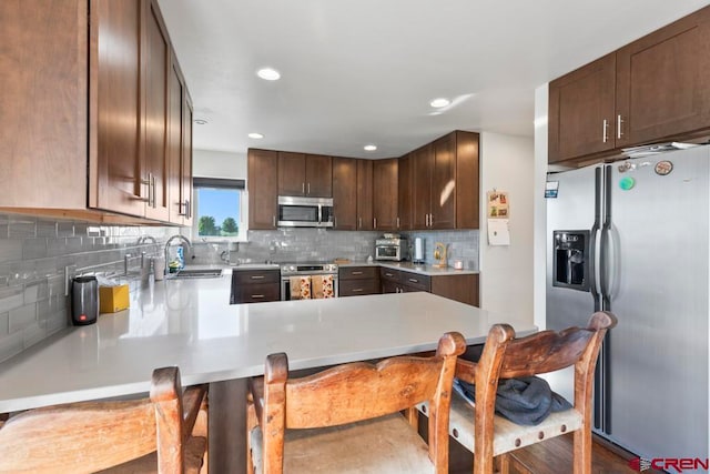 kitchen with sink, kitchen peninsula, a kitchen bar, decorative backsplash, and appliances with stainless steel finishes