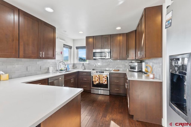 kitchen featuring tasteful backsplash, sink, kitchen peninsula, appliances with stainless steel finishes, and dark hardwood / wood-style flooring