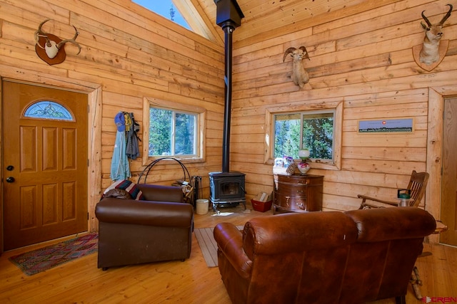 living room featuring high vaulted ceiling, a wood stove, light wood-type flooring, and wooden walls