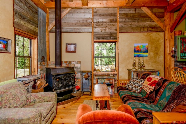 living room featuring a wood stove, beamed ceiling, light wood-type flooring, and a healthy amount of sunlight