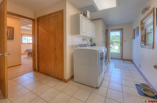 laundry room with separate washer and dryer, light tile patterned floors, and cabinets