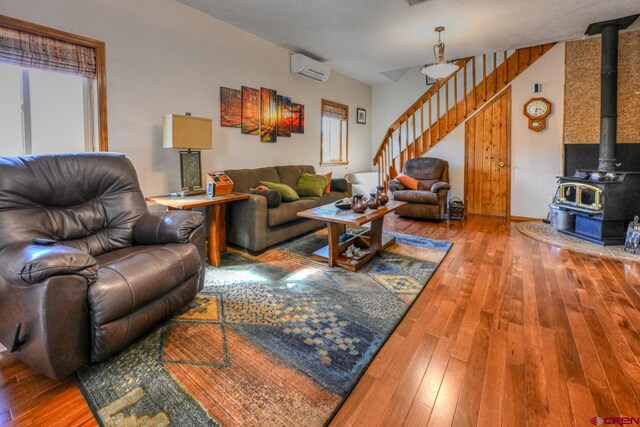 living room with wood-type flooring, a wall mounted AC, a wood stove, and a wealth of natural light