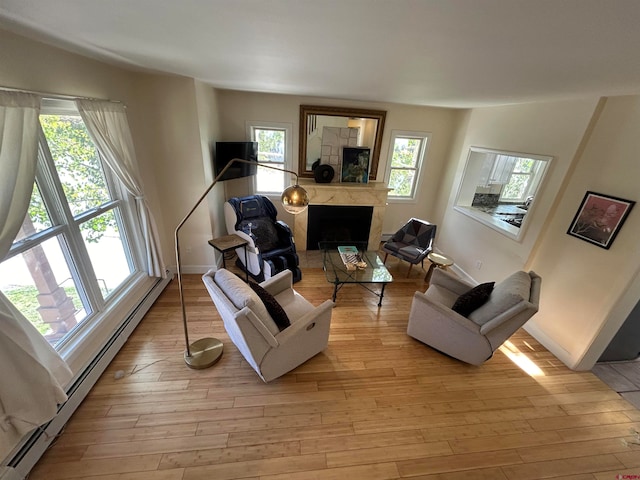 living room with light hardwood / wood-style floors, plenty of natural light, a high end fireplace, and a baseboard radiator