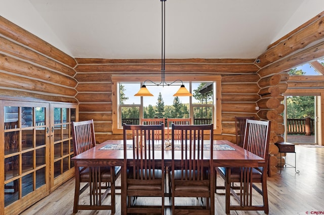 dining area featuring wood-type flooring, vaulted ceiling, and rustic walls