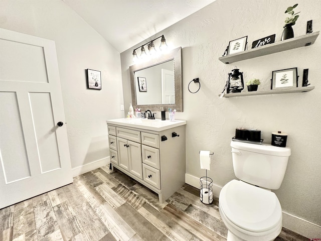 bathroom with toilet, vanity, vaulted ceiling, and wood finished floors