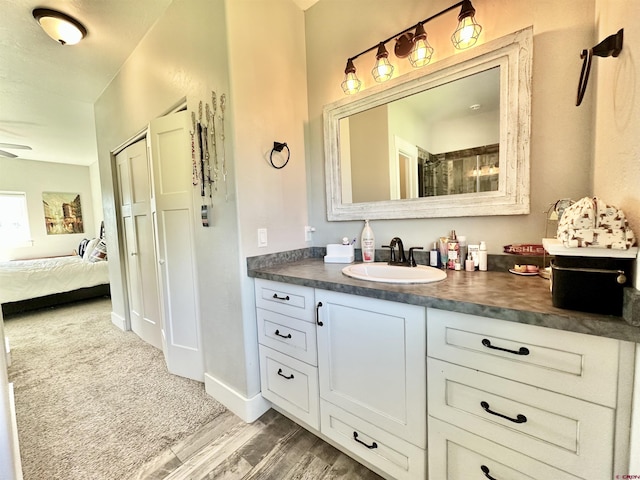 ensuite bathroom with vanity, wood finished floors, ensuite bath, baseboards, and ceiling fan