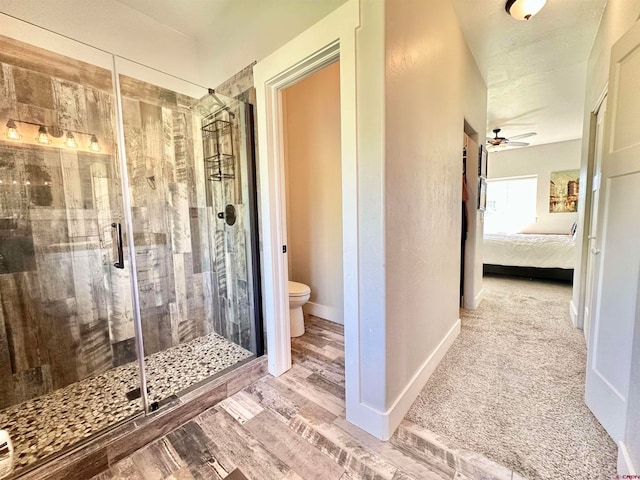 bathroom with hardwood / wood-style flooring, toilet, ceiling fan, and an enclosed shower