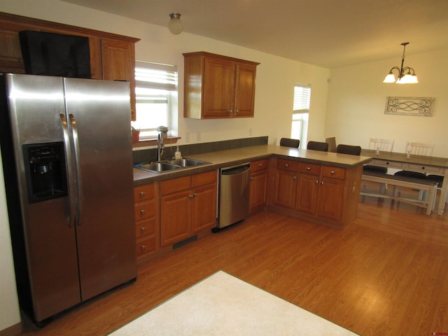 kitchen with sink, kitchen peninsula, light hardwood / wood-style flooring, a chandelier, and appliances with stainless steel finishes