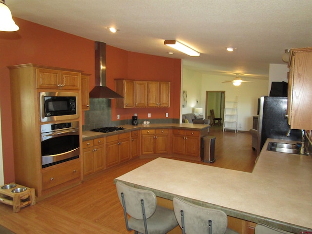 kitchen with wall chimney exhaust hood, sink, stainless steel appliances, and kitchen peninsula