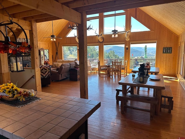 dining room featuring ceiling fan, a mountain view, beamed ceiling, wood walls, and high vaulted ceiling