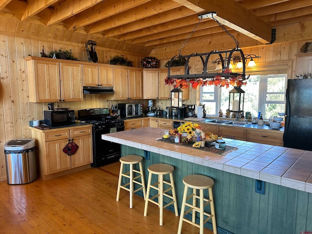 kitchen featuring black appliances, wood walls, beamed ceiling, and tile countertops