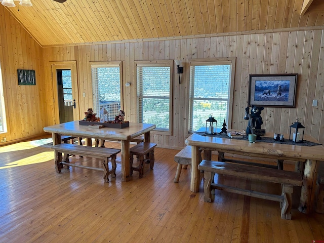 dining area with light hardwood / wood-style flooring, wooden walls, vaulted ceiling, and wooden ceiling