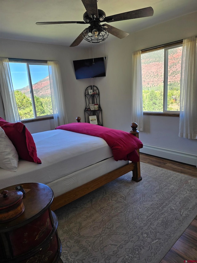 bedroom with ceiling fan, hardwood / wood-style flooring, and a baseboard heating unit