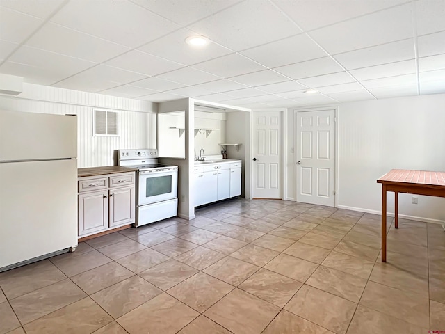 kitchen with white cabinets, light tile patterned floors, sink, white appliances, and a drop ceiling