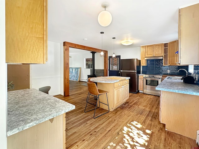 kitchen with appliances with stainless steel finishes, a breakfast bar, a kitchen island, pendant lighting, and light hardwood / wood-style flooring