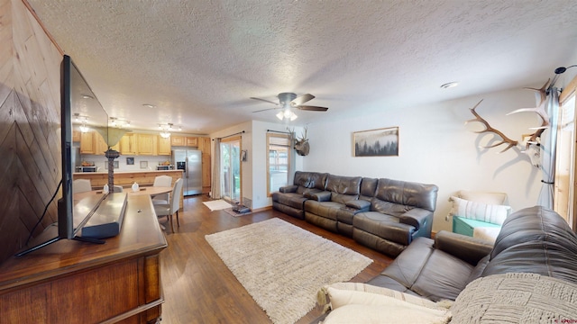 living room with ceiling fan, a textured ceiling, and dark hardwood / wood-style floors