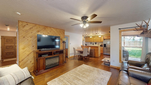 living room featuring wood walls, ceiling fan, hardwood / wood-style flooring, and a textured ceiling