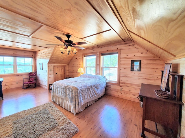 bedroom featuring multiple windows, light hardwood / wood-style floors, wood walls, and ceiling fan