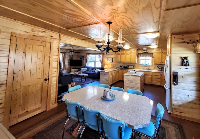 kitchen featuring fridge, wooden walls, a center island, and a notable chandelier