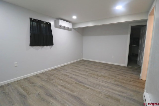 basement featuring light hardwood / wood-style floors, baseboard heating, and a wall mounted air conditioner