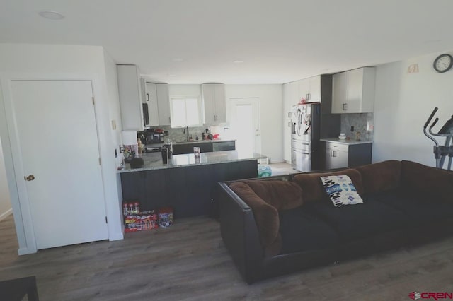 kitchen with wood-type flooring, kitchen peninsula, stainless steel refrigerator, decorative backsplash, and light stone countertops