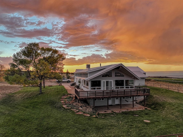 back house at dusk featuring a lawn, a deck, and a patio area