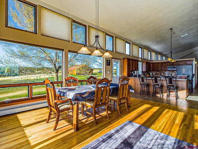 dining room featuring lofted ceiling, hardwood / wood-style floors, and a baseboard heating unit