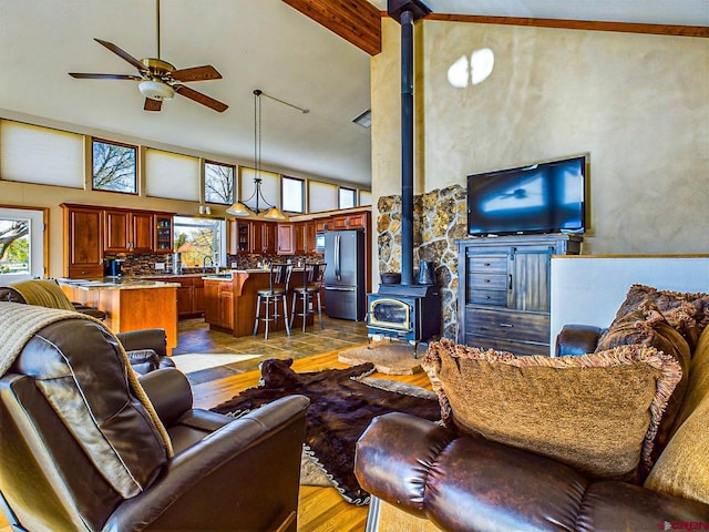 living room featuring high vaulted ceiling, a wood stove, beam ceiling, ceiling fan, and light hardwood / wood-style flooring