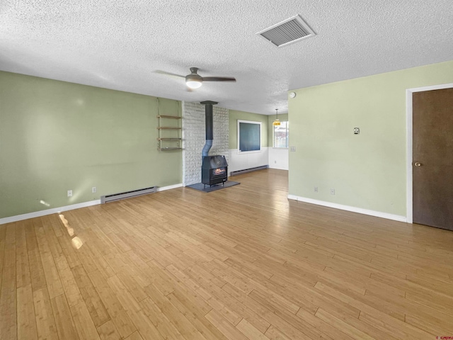 unfurnished living room featuring a wood stove, light hardwood / wood-style floors, and a textured ceiling