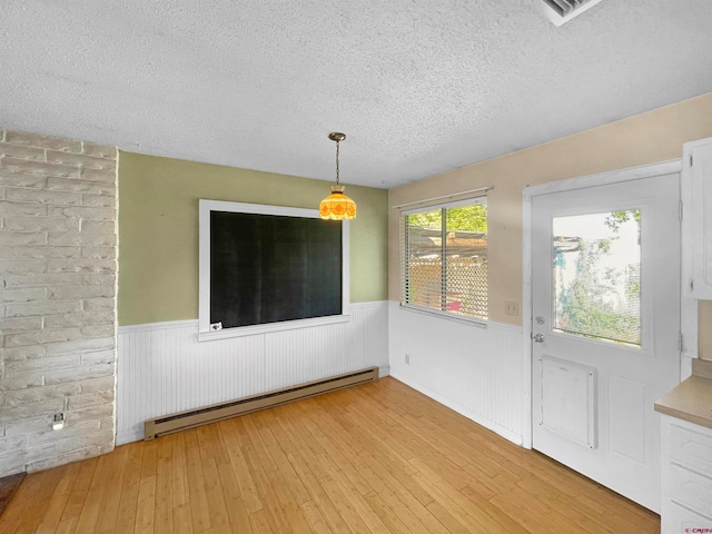 unfurnished dining area with a baseboard radiator, hardwood / wood-style floors, and a textured ceiling