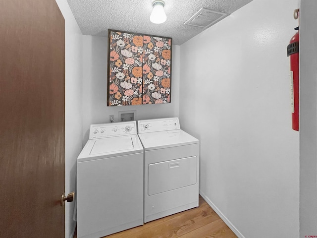 laundry area featuring a textured ceiling, independent washer and dryer, and light hardwood / wood-style flooring