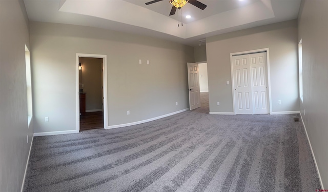 unfurnished bedroom featuring a closet, ceiling fan, a raised ceiling, and dark carpet