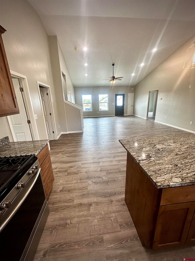 kitchen featuring hardwood / wood-style floors, dark stone countertops, gas stove, and ceiling fan