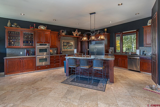 kitchen with hanging light fixtures, dark stone countertops, a breakfast bar, stainless steel appliances, and a kitchen island with sink