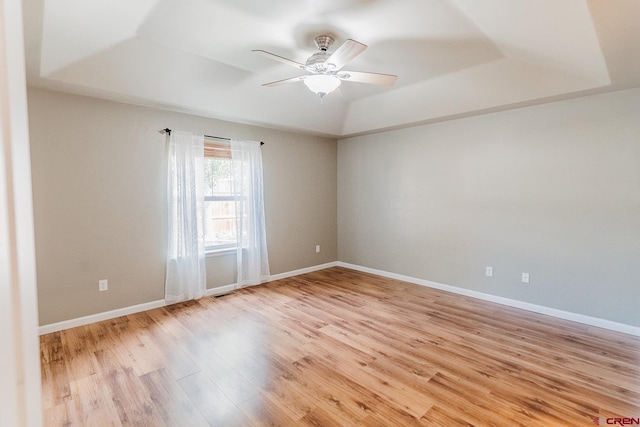 empty room with light hardwood / wood-style flooring, ceiling fan, and a raised ceiling