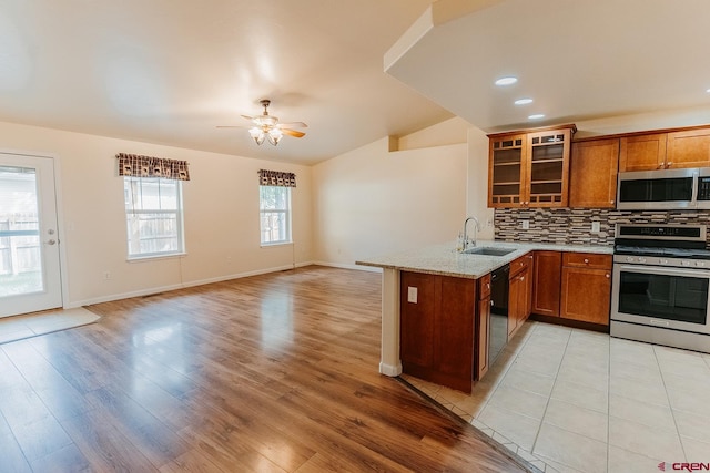 kitchen featuring lofted ceiling, kitchen peninsula, tasteful backsplash, stainless steel appliances, and light hardwood / wood-style floors