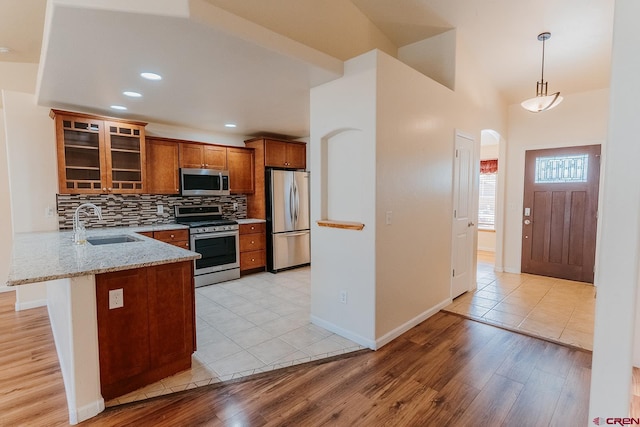 kitchen featuring light wood-type flooring, light stone counters, kitchen peninsula, and appliances with stainless steel finishes