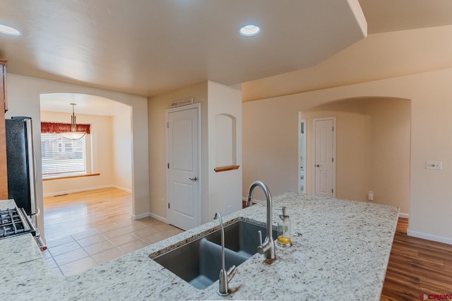 kitchen with wood-type flooring, light stone counters, decorative light fixtures, and sink