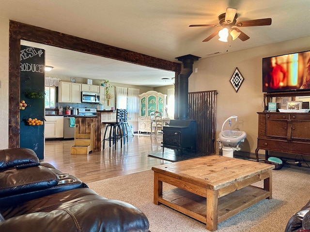 living room with ceiling fan, light hardwood / wood-style floors, and a wood stove