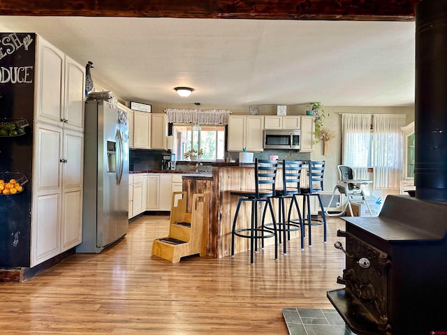 kitchen featuring decorative backsplash, a wood stove, stainless steel appliances, a textured ceiling, and light hardwood / wood-style flooring