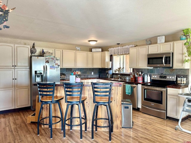 kitchen with a textured ceiling, stainless steel appliances, cream cabinetry, and light hardwood / wood-style flooring