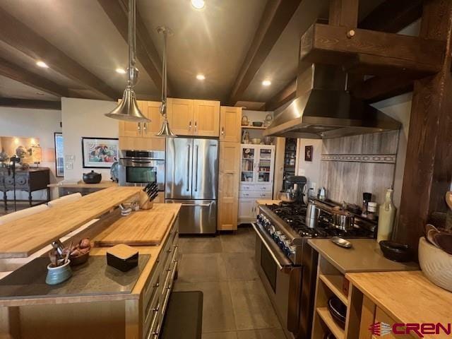 kitchen with a kitchen island, stainless steel appliances, beam ceiling, dark tile patterned floors, and wall chimney range hood