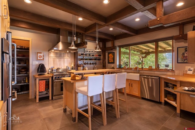 kitchen with appliances with stainless steel finishes, a breakfast bar, wall chimney exhaust hood, beam ceiling, and wood counters