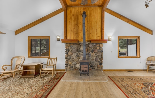 sitting room featuring wood finished floors, a wood stove, lofted ceiling with beams, and baseboards
